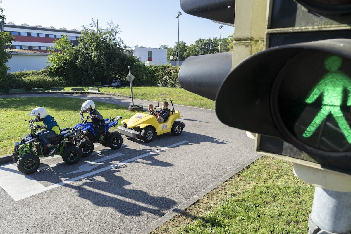 Kiddi-Car Kinderverkehrstraining Osterferien 2023 in Bayern 1 Grüne Fußgängerampel mit Kinderfahrzeugen im Hintergrund auf Verkehrsübungsplatz